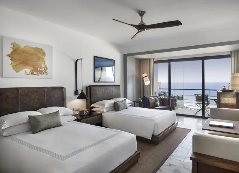 Chambre lumineuse avec deux lits et vue sur la mer par de grandes baies vitrées.