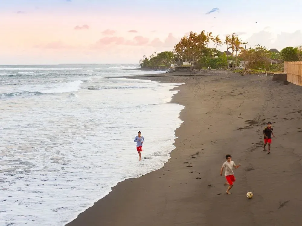 Une plage de sable sombre avec des personnes se baignant et jouant au football.