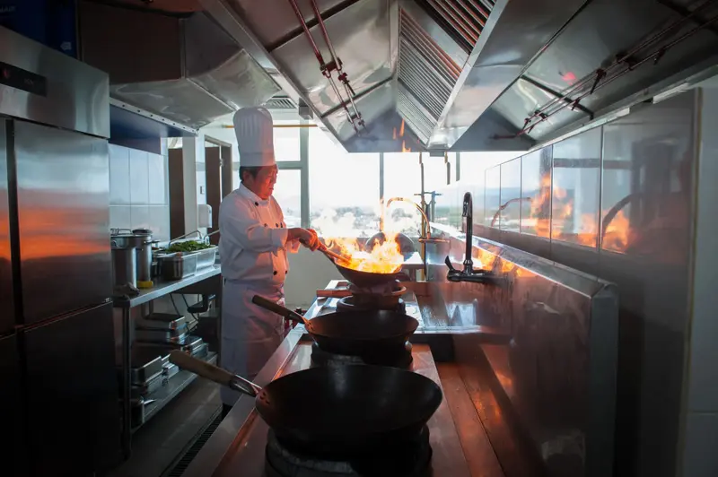 Un chef cuisinier prépare des plats avec des flammes dans une cuisine professionnelle.