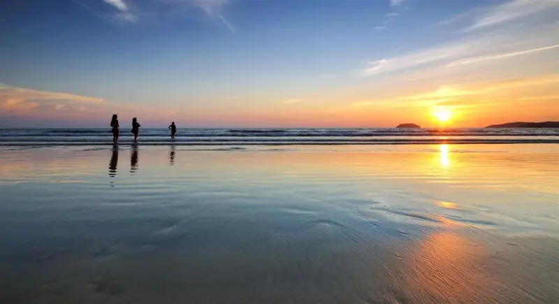 Trois silhouettes se promènent sur une plage au coucher du soleil.