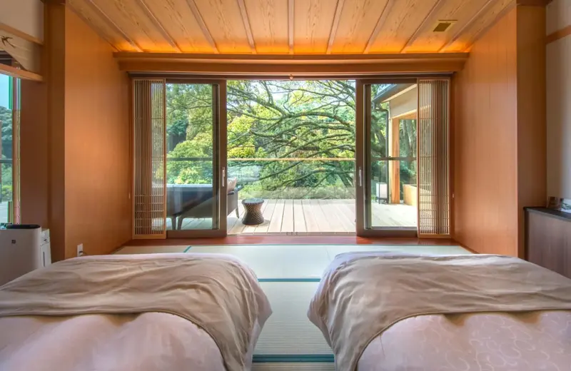 Une chambre lumineuse donne sur une terrasse en bois et une végétation luxuriante.