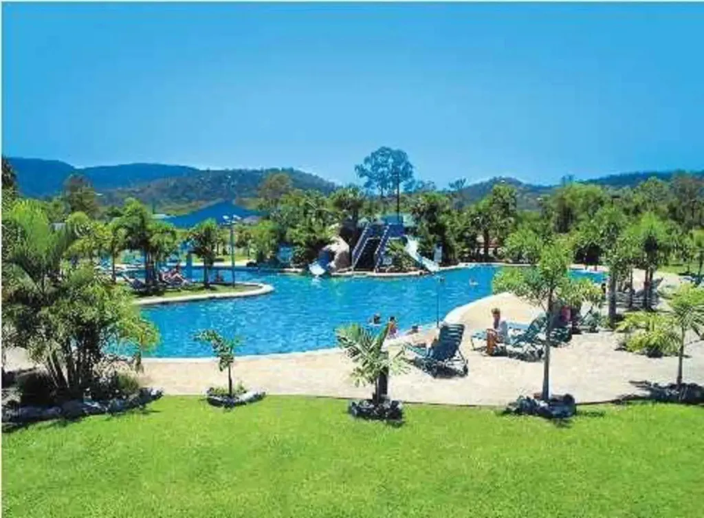 Une piscine bordée de transats et de palmiers, avec une cascade et un toboggan.
