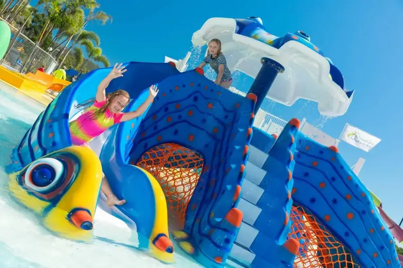 Des enfants glissent sur un toboggan aquatique coloré dans une piscine ensoleillée.