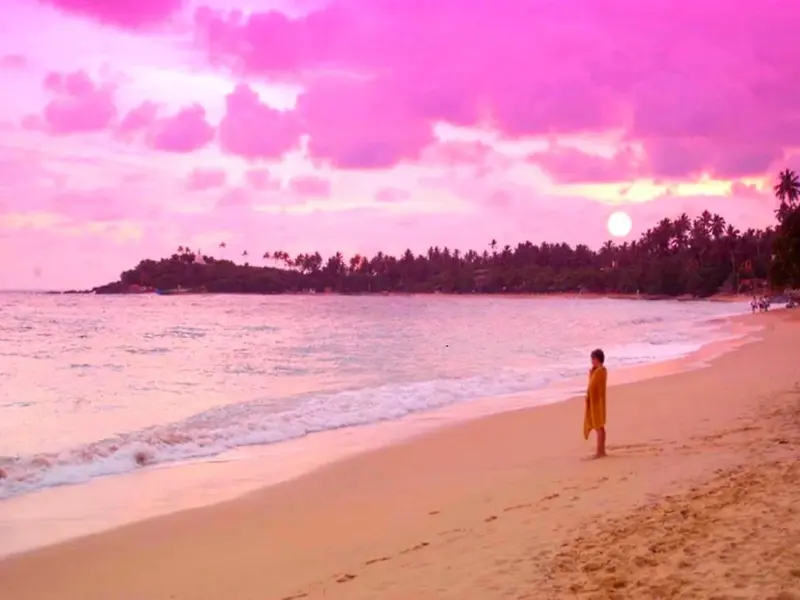 Une personne se promène sur une plage de sable fin au coucher du soleil.