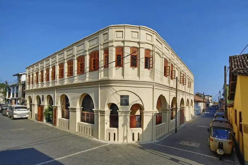 Bâtiment beige à deux étages avec des fenêtres à volets marron et des arches.