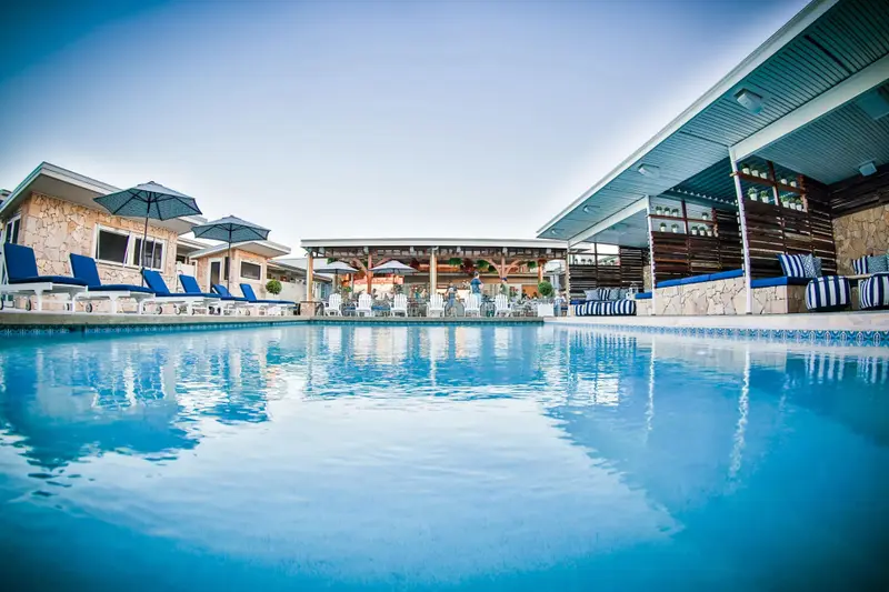 Une piscine turquoise reflète le ciel bleu et les bâtiments environnants.