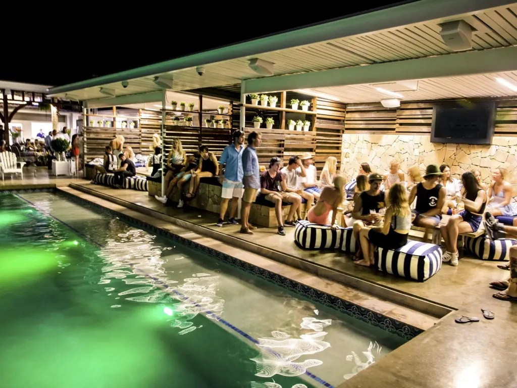 Des clients discutent et se détendent près d'une piscine illuminée en soirée.