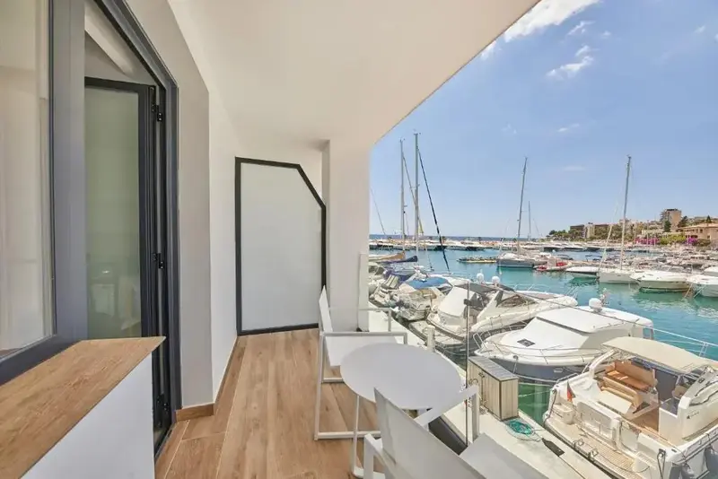 Terrasse avec mobilier blanc donnant sur un port de plaisance ensoleillé.