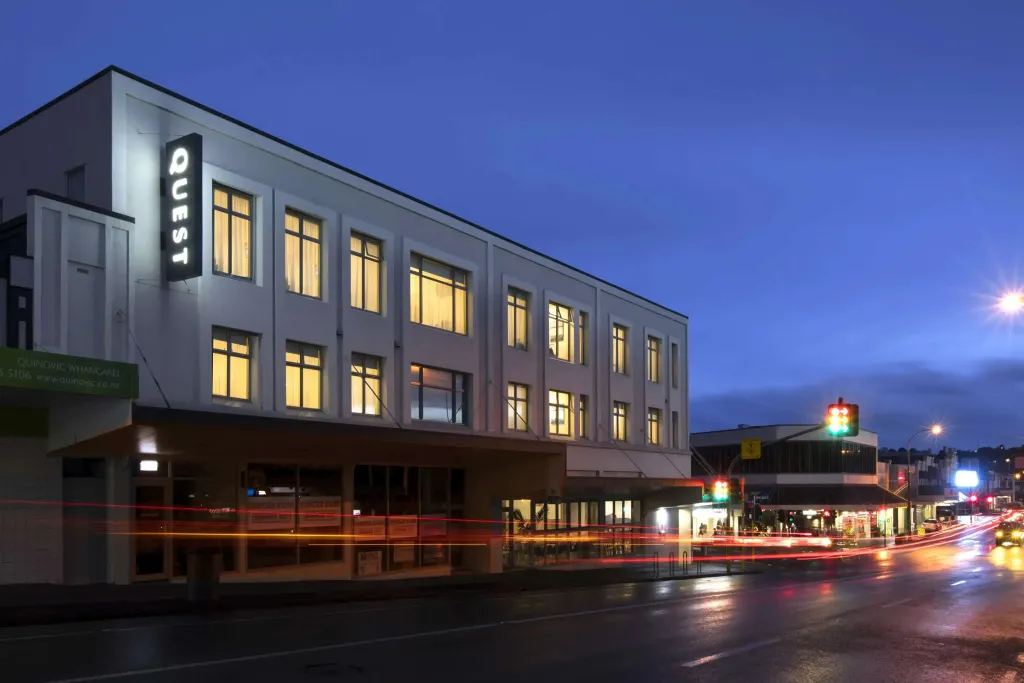 Bâtiment moderne éclairé la nuit avec des fenêtres illuminées et une rue animée.