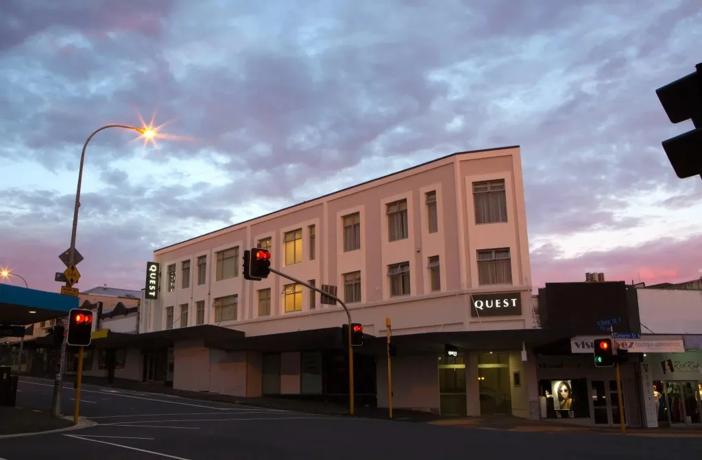 Bâtiment blanc à plusieurs étages illuminé sous un ciel nuageux au crépuscule.
