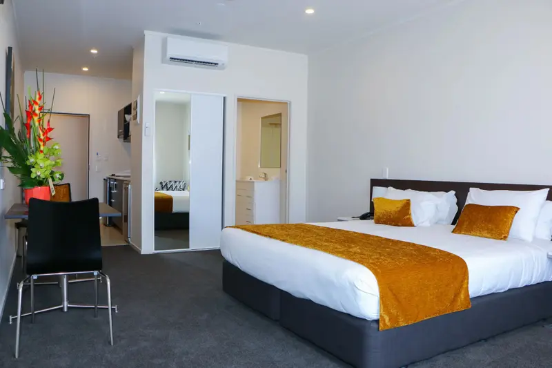 Une chambre lumineuse avec un grand lit recouvert d'une courtepointe jaune et de coussins.