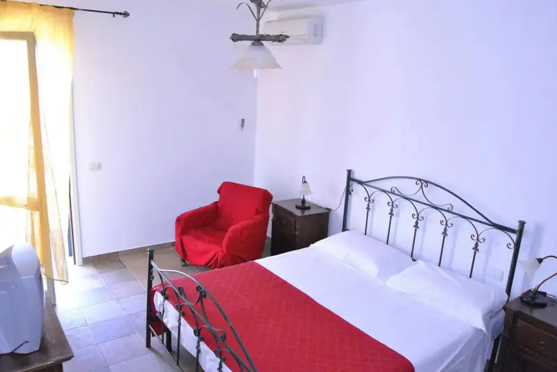 Une chambre lumineuse avec un lit recouvert d'une couverture rouge et un fauteuil.