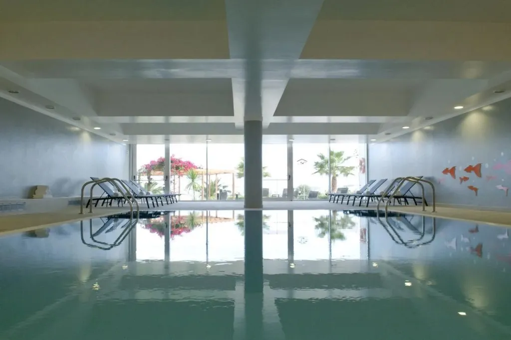 Une piscine intérieure avec des transats alignés le long d'une baie vitrée.