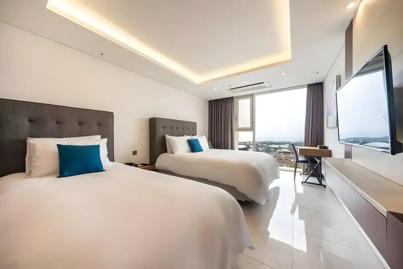 Une chambre lumineuse avec deux lits simples et une vue sur la ville.