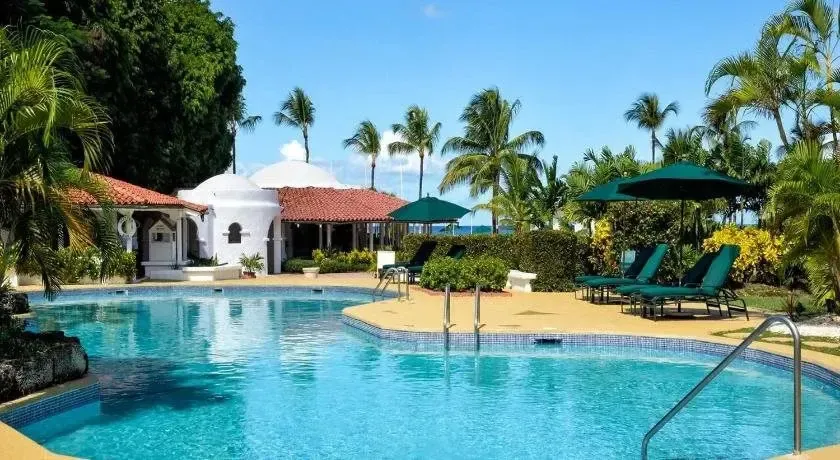 Une piscine turquoise bordée de transats verts sous des parasols, entourée d'une végétation luxuriante.