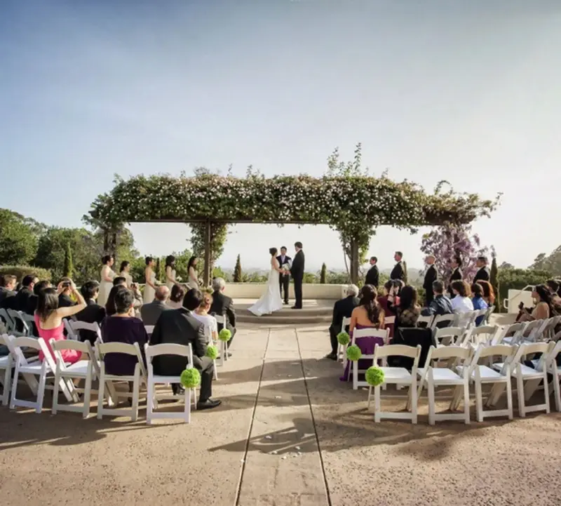 Cérémonie de mariage en extérieur avec une arche fleurie et des invités assis sur des chaises.