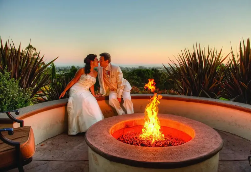 Un couple s'embrasse près d'un foyer extérieur avec une vue sur le paysage au coucher du soleil.