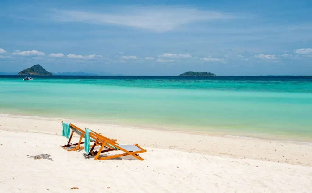 Deux transats bleus sur une plage de sable blanc bordée d'une mer turquoise.