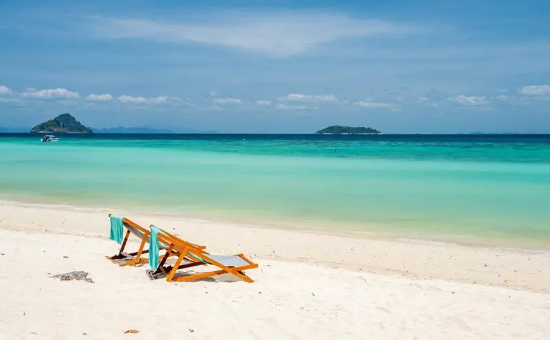 Deux transats bleus sur une plage de sable blanc bordée d'une mer turquoise.