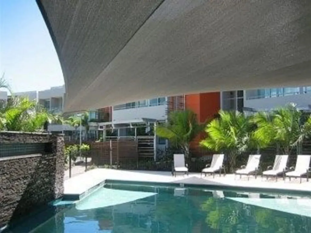 Transats alignés au bord d'une piscine ombragée par une voile.