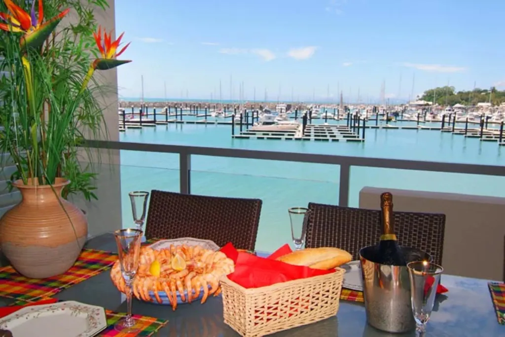 Une table dressée avec des fruits de mer et du champagne offre une vue sur un port de plaisance ensoleillé.
