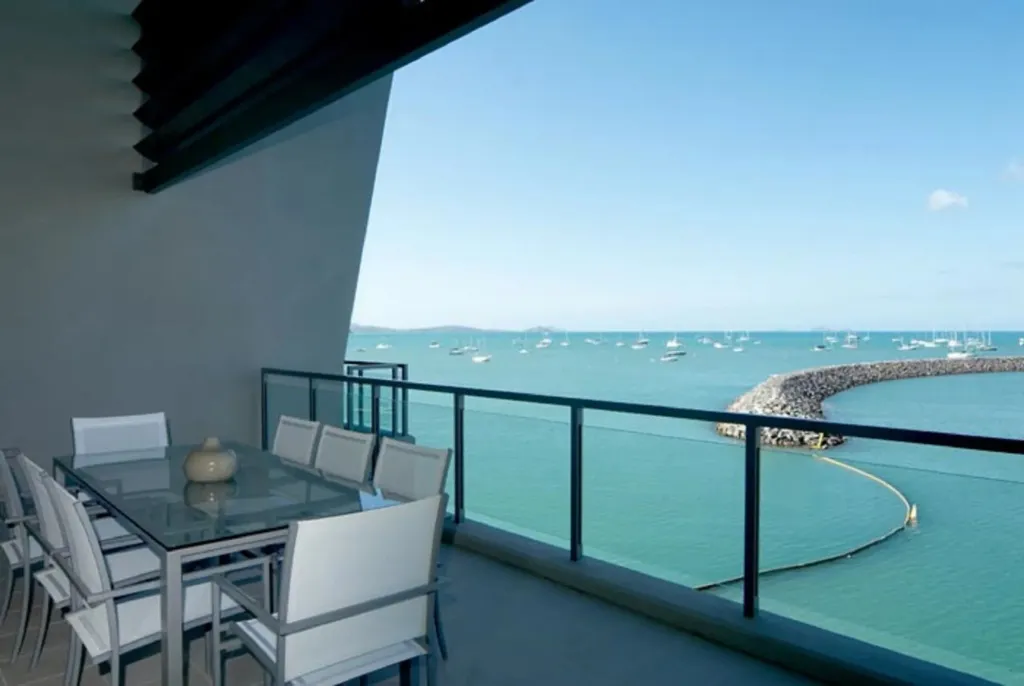Une table à manger est installée sur une terrasse avec vue sur la mer et des bateaux.
