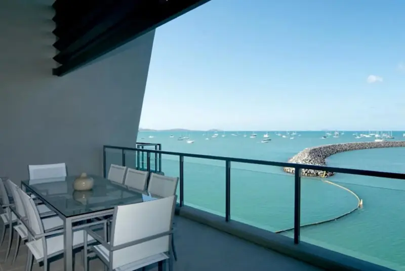 Une table à manger est installée sur une terrasse avec vue sur la mer et des bateaux.