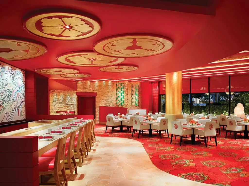 Une salle de restaurant spacieuse aux tons rouges et dorés, avec des tables dressées et un décor floral au plafond.