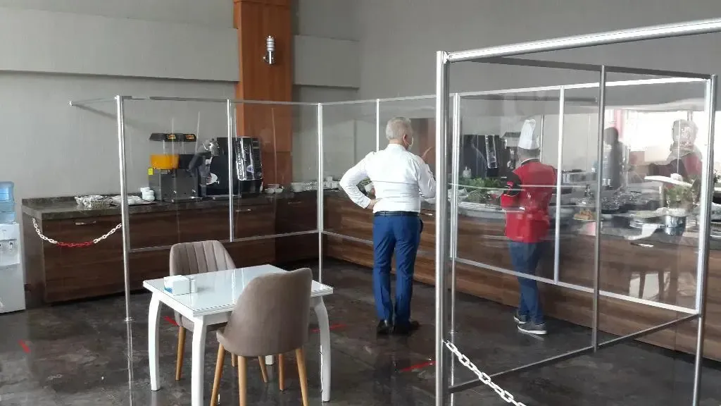Un buffet de nourriture est visible derrière une paroi protectrice, avec un client debout.