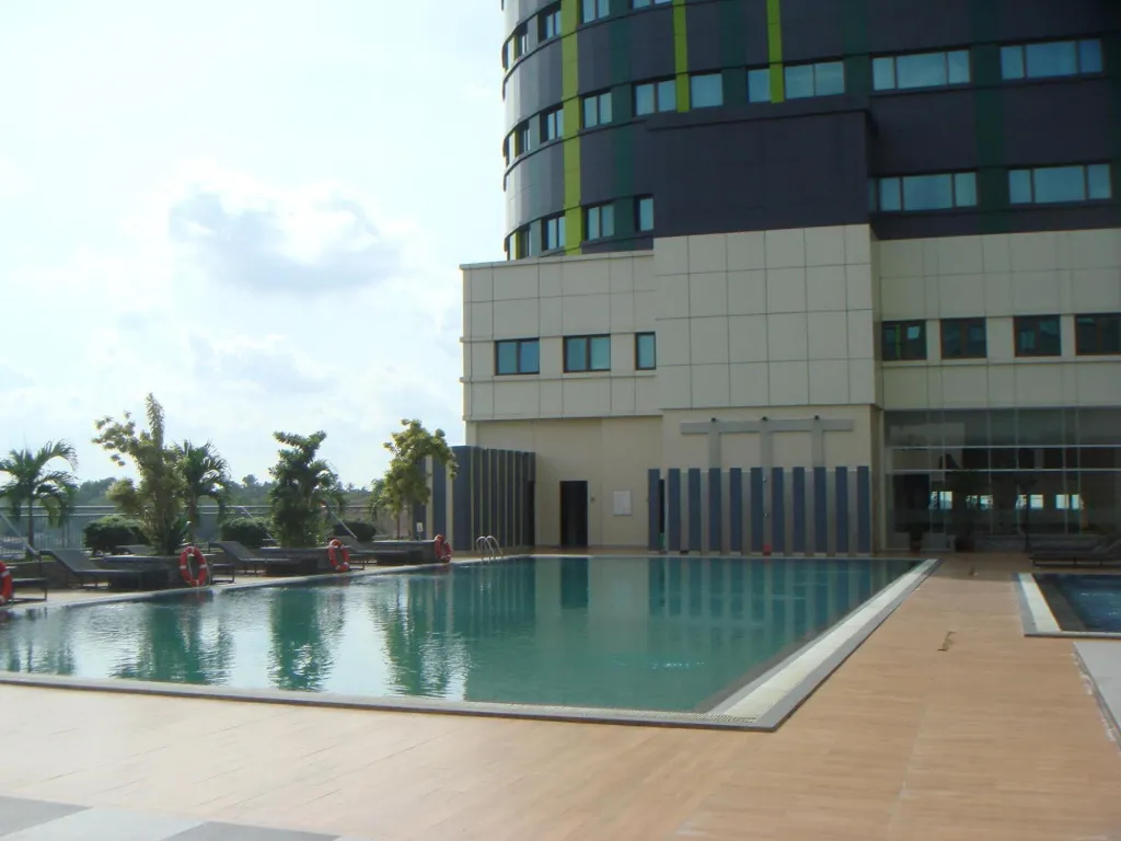 Une piscine rectangulaire avec une terrasse carreee et un batiment moderne en fond.