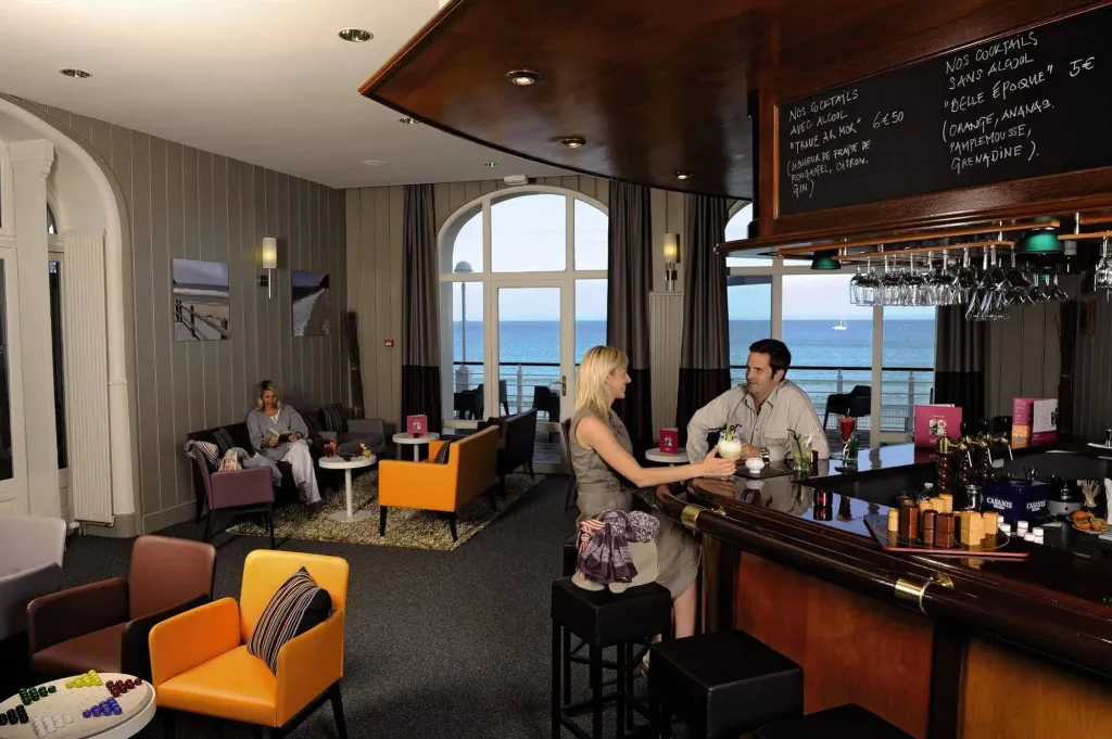 Un bar avec des clients et une vue sur la mer par de grandes fenêtres.