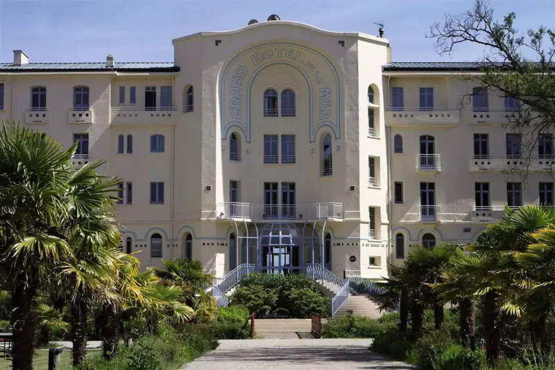 Façade d'un grand bâtiment beige avec des palmiers devant.