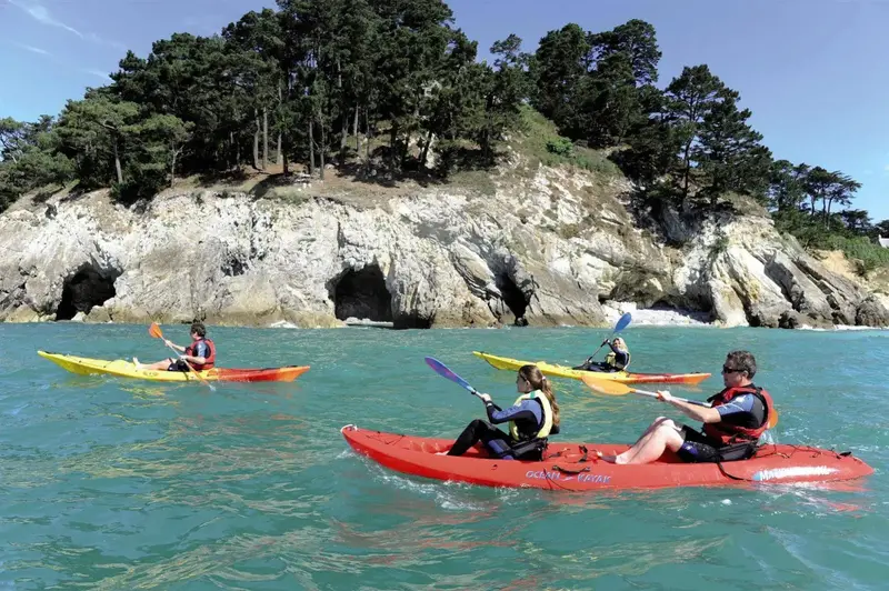 Des kayaks naviguent sur une eau turquoise face à une côte rocheuse et boisée.