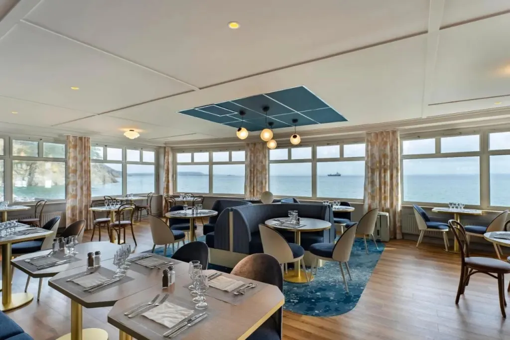 Une salle lumineuse avec de grandes baies vitrées donnant sur la mer.