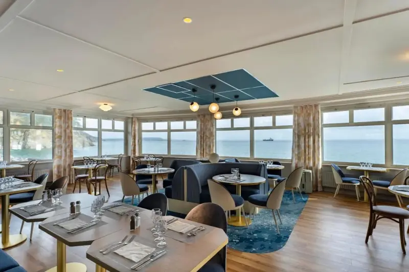 Une salle lumineuse avec de grandes baies vitrées donnant sur la mer.