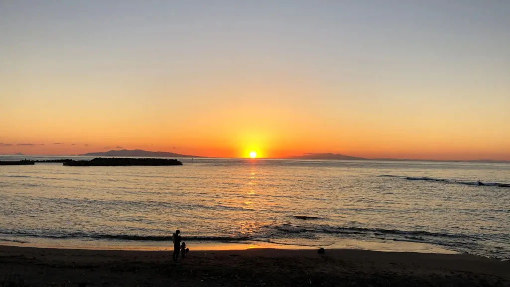 Coucher de soleil sur la mer avec une plage au premier plan.