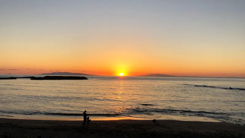 Coucher de soleil sur la mer avec une plage au premier plan.