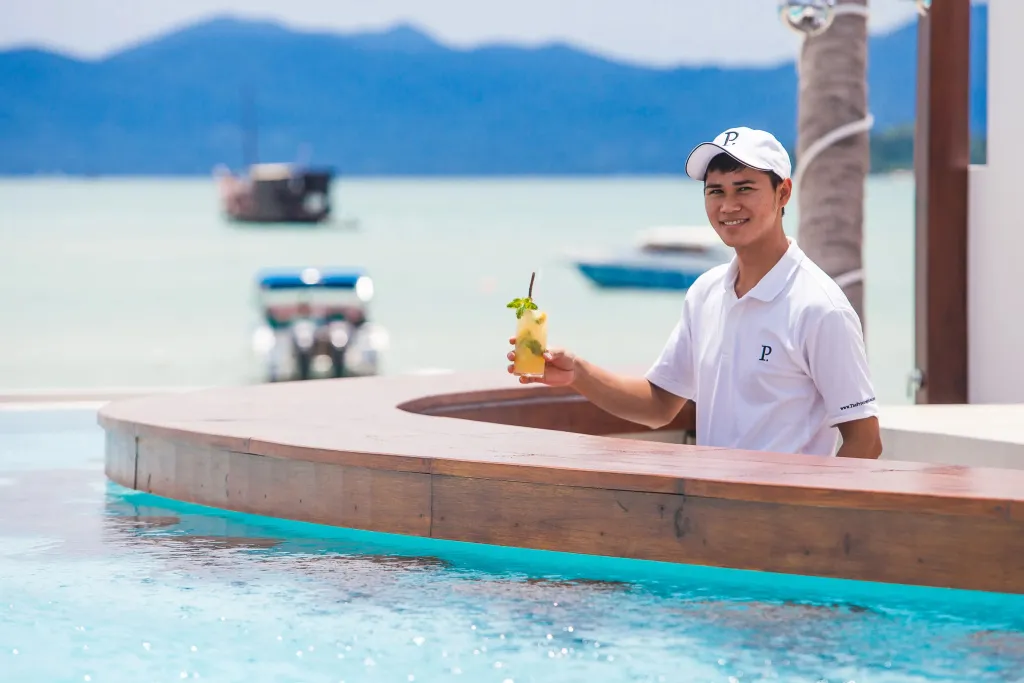 Un serveur souriant présente une boisson rafraîchissante au bord d'une piscine.