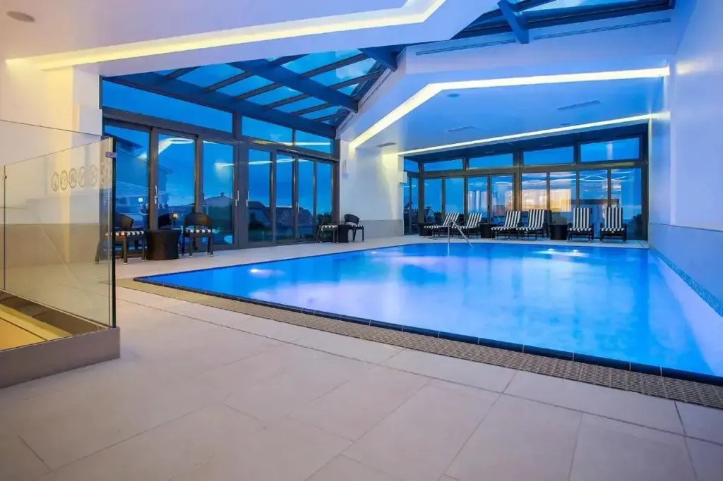 Une piscine intérieure lumineuse avec des transats alignés près de grandes baies vitrées.