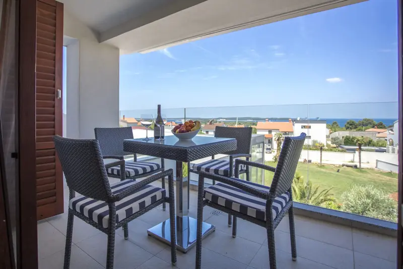 Une table et des chaises se trouvent sur un balcon avec vue sur la mer et la végétation.