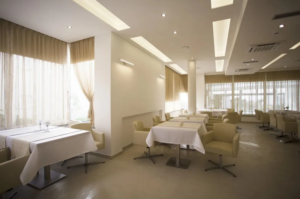 Une salle lumineuse est aménagée avec des tables nappées et des chaises confortables.