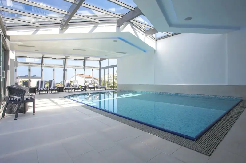 Une piscine intérieure lumineuse avec des transats et de grandes baies vitrées.