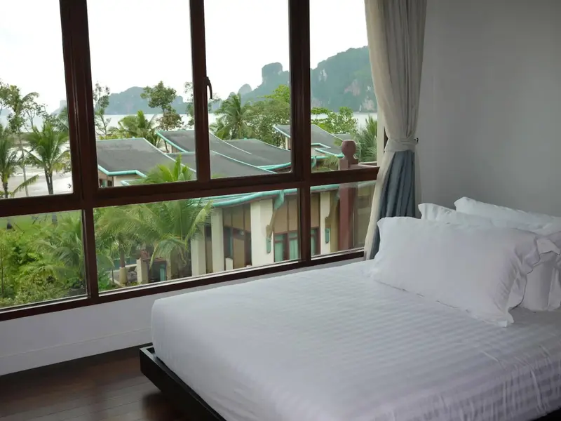 Une chambre lumineuse avec un grand lit face à une vue sur la mer et la végétation.