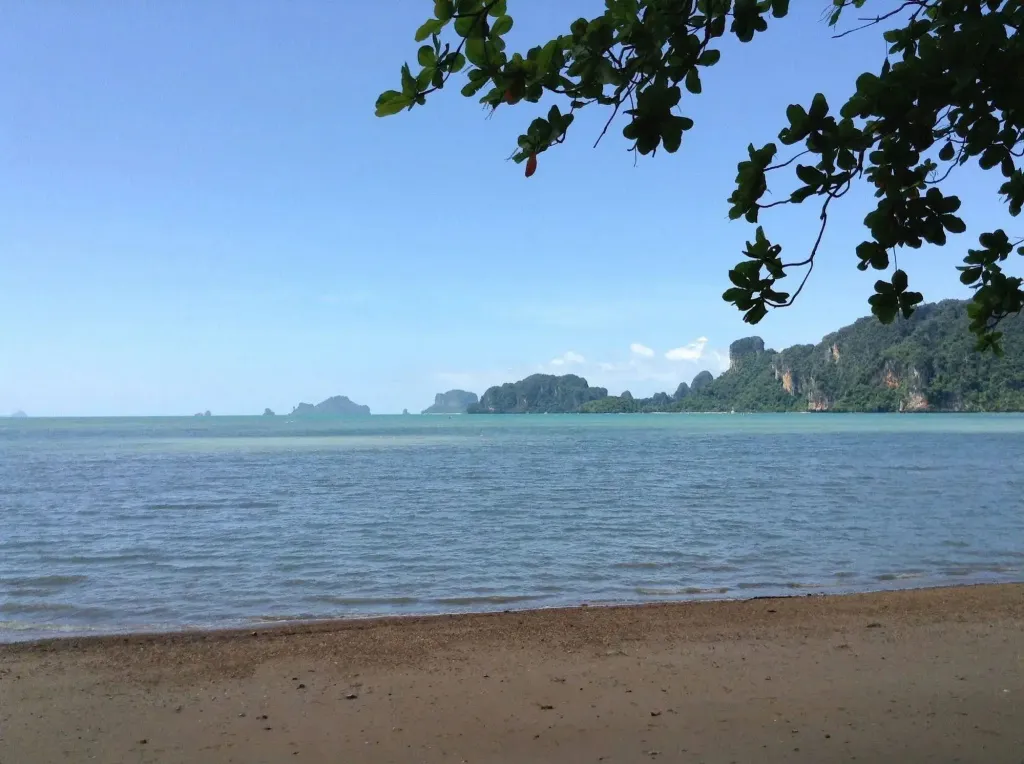 Plage de sable fin bordée d'une mer calme et d'îles verdoyantes.