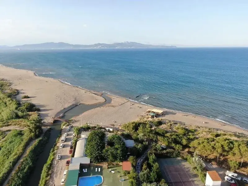 Vue aérienne d'une plage de sable bordée de végétation et d'un établissement avec piscine.