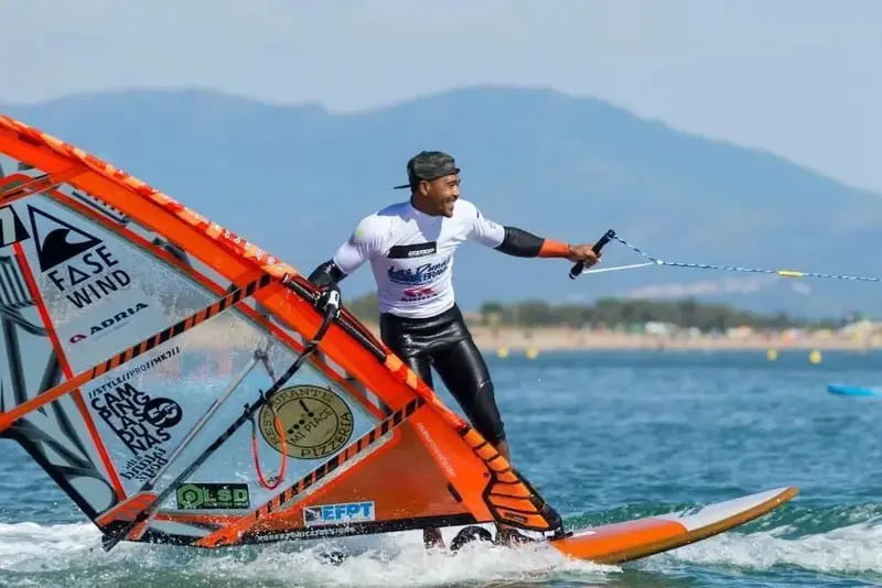 Un homme pratique la planche à voile sur une mer agitée sous un ciel bleu.
