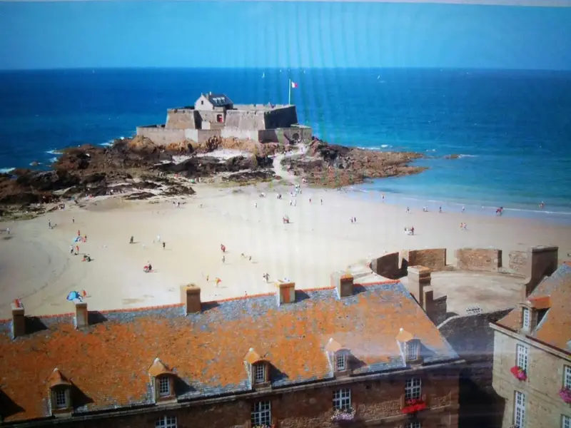 Vue d'une plage de sable fin avec un fort au loin.