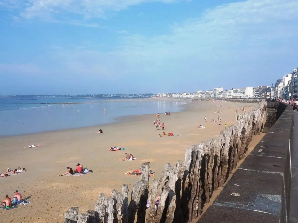 Une plage de sable fin avec des baigneurs et des parasols sous un ciel bleu.