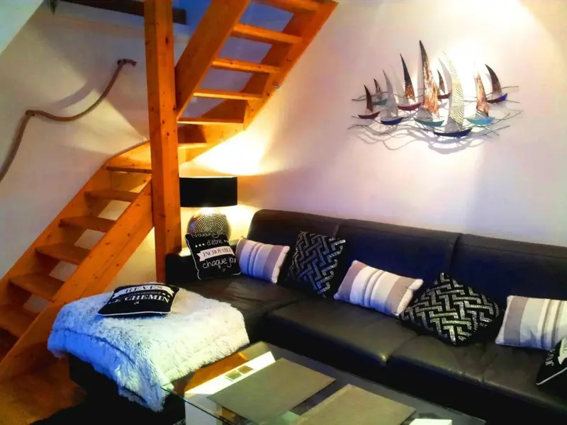 Un canapé noir et des coussins reposent devant un escalier en bois.
