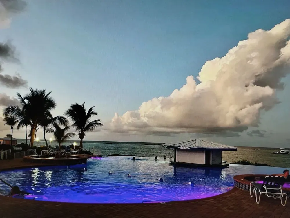 Piscine illuminée avec bar intégré et vue sur la mer au coucher du soleil.